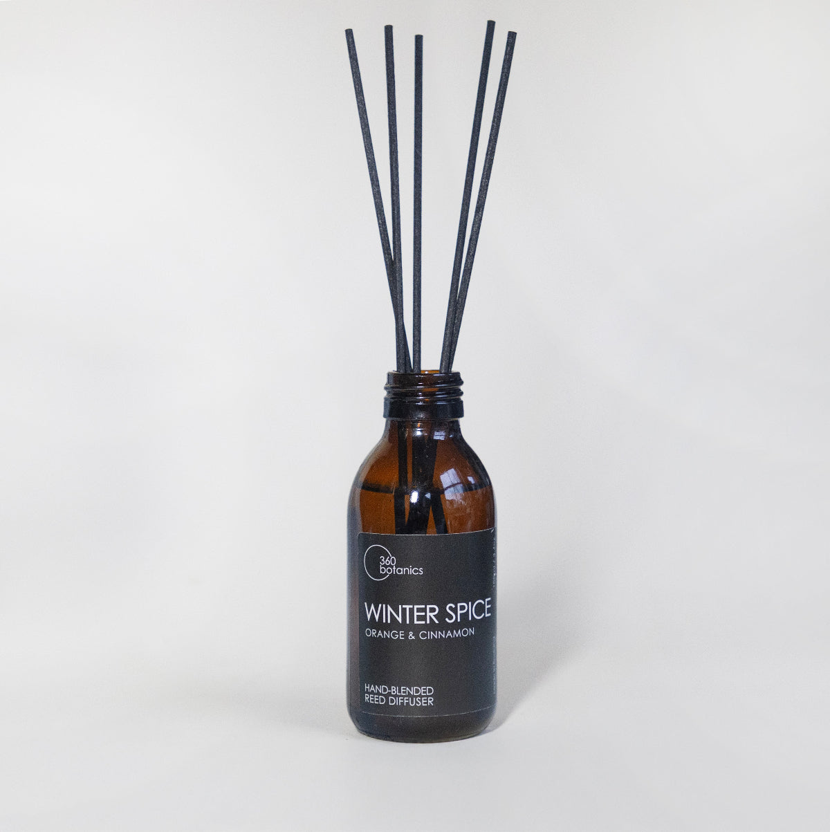 360 Botanics Winter Spice Reed Diffuser with natural orange and cinnamon fragrance, presented in an amber glass bottle with black reeds for a cozy and festive home atmosphere.