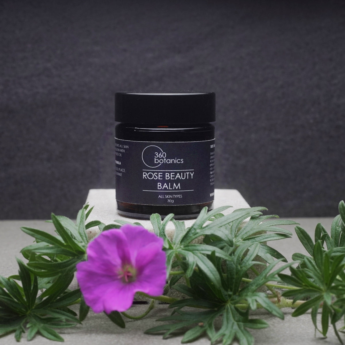 A jar of 360 Botanics Rose Beauty Balm displayed with a vibrant purple flower and green leaves. A natural, vegan, and hydrating skincare product