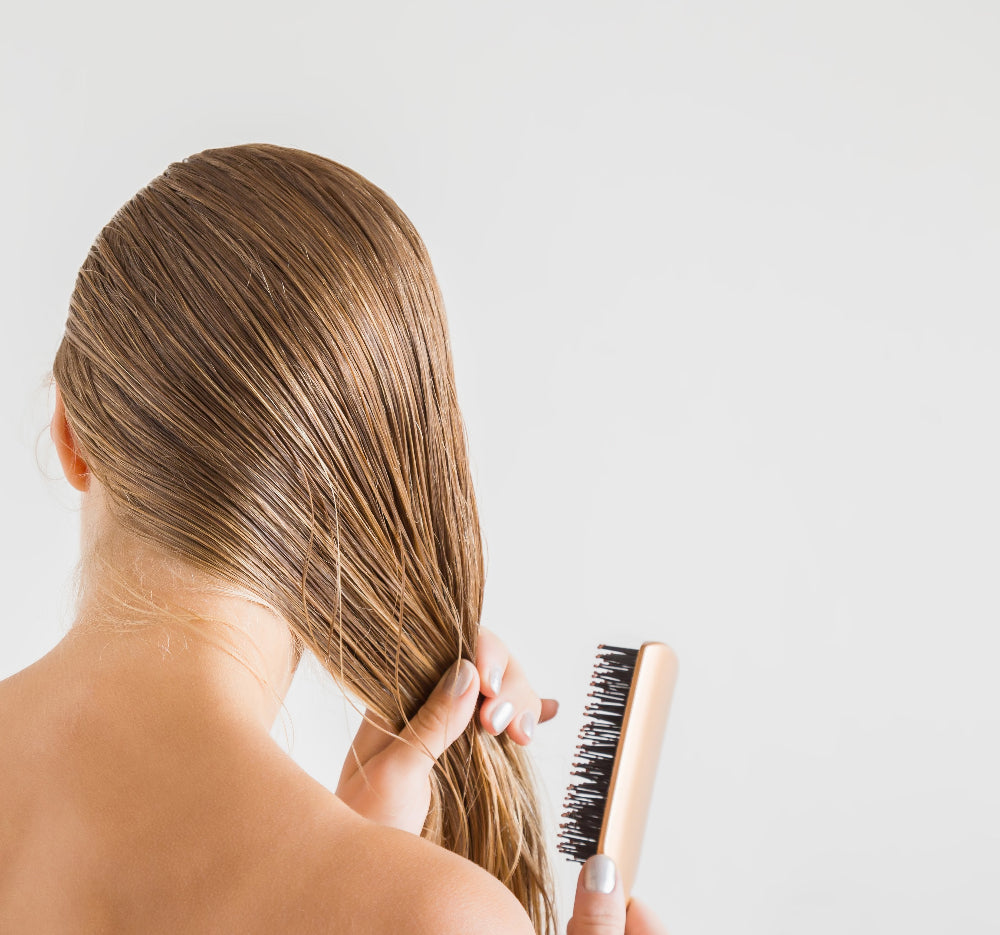 A woman gently brushing her long, smooth hair, freshly conditioned with 360 Botanics Botanica Organic Conditioner. The minimalist bathroom setting reflects a serene and natural hair care ritual, highlighting radiant, healthy hair.