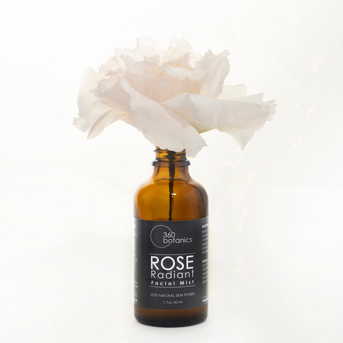 A bottle of 360 Botanics Rose Radiant Facial Mist labeled as 100% natural skin toner in a 1.7 oz or 50 ml size, with a single large white rose flower emerging from the top, set against a white background.