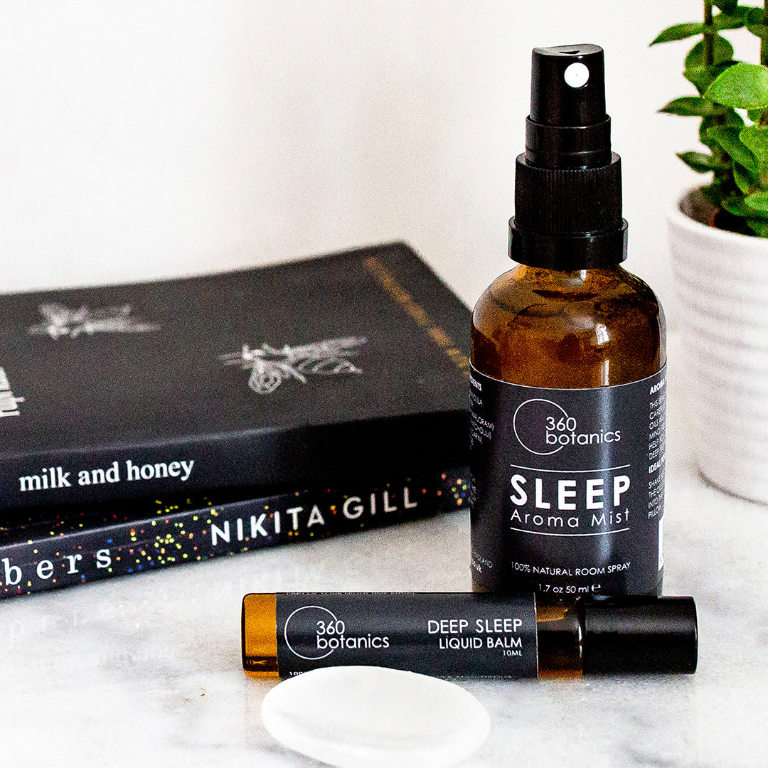 sleep aroma mist spray amber bottle black lid, green plant, two books, marble surface