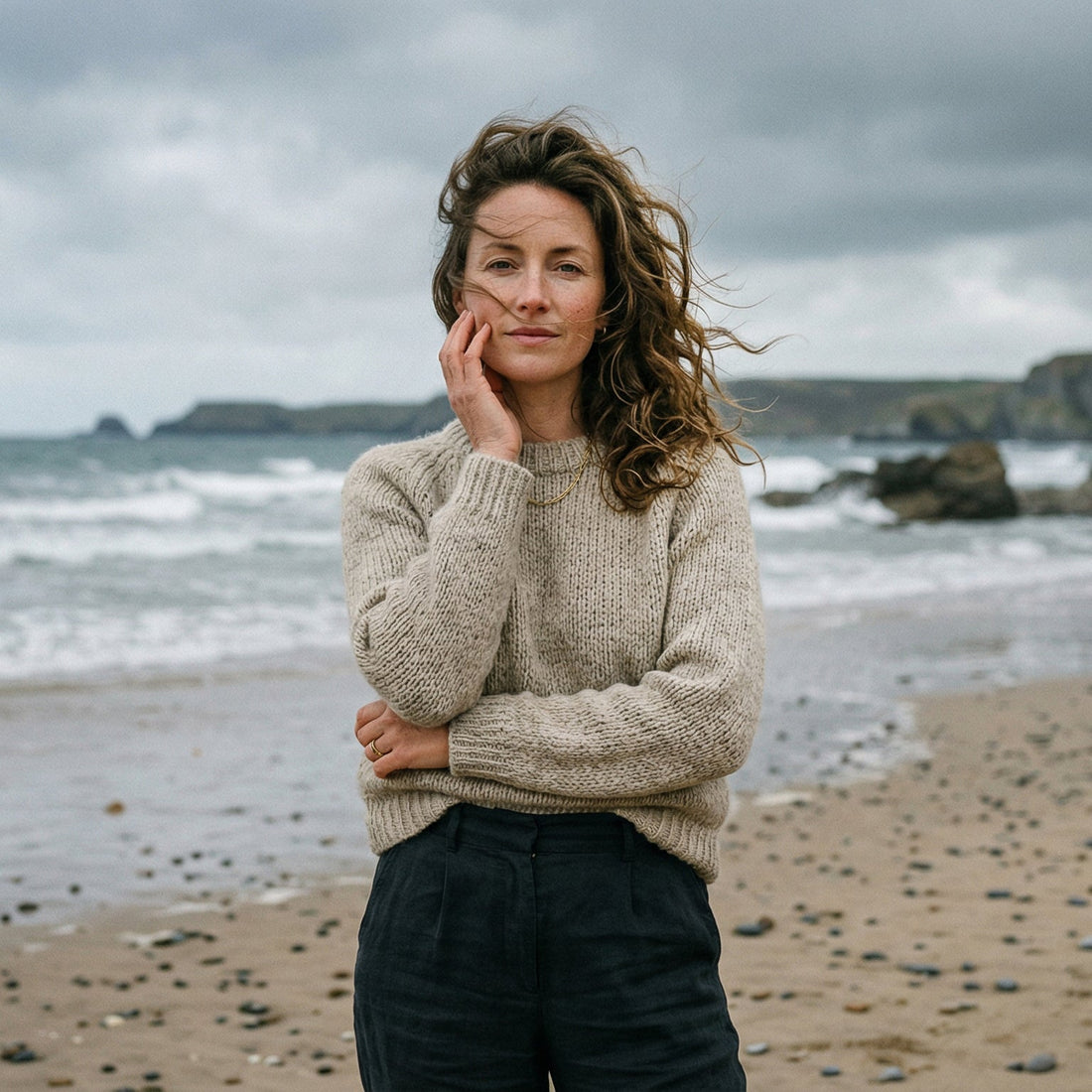 Woman on a windy English beach touching her face, illustrating the effects of salt water and sea air on skin.