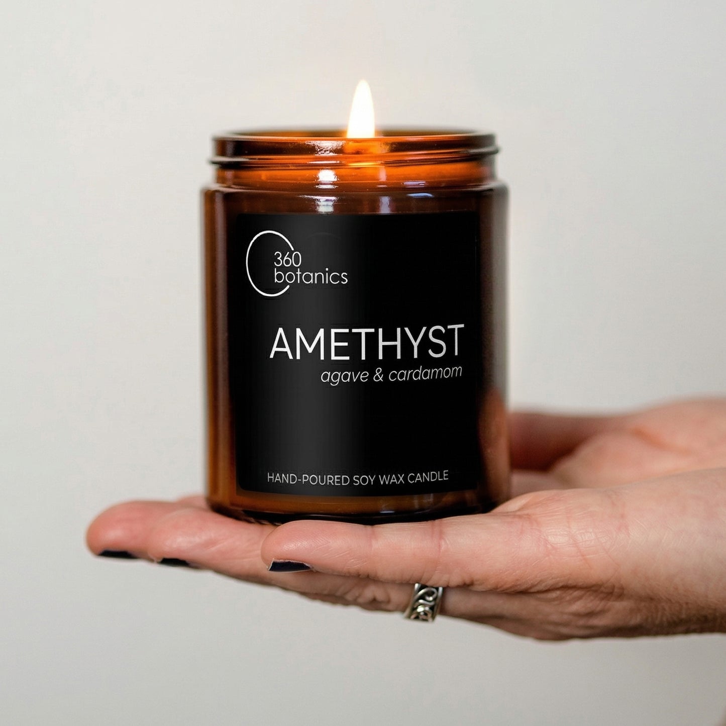 Candle in an amber jar labeled 'Amethyst' held in a hand against a neutral background