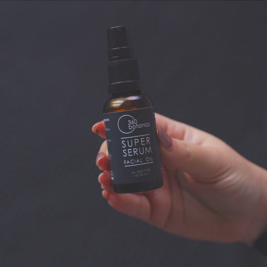 Close-up video of a hand holding a 30ml bottle of 360 Botanics Super Serum Facial Oil. The bottle features a sleek black label and pump dispenser, shown against a dark, smooth background, highlighting the product's design