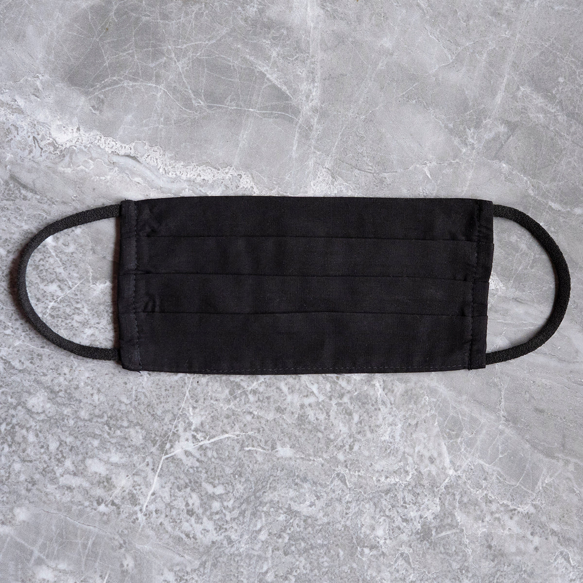 A plain black cloth face mask displayed on a textured marble background, highlighting a simple and essential health accessory.