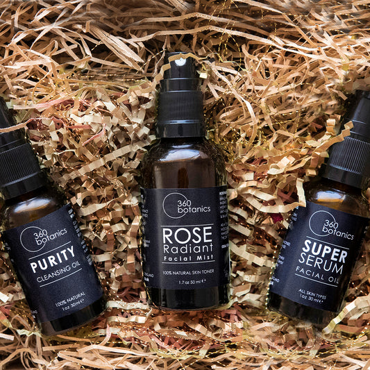 Three 360 Botanics skincare products nestled in shredded paper: Purity Cleansing Oil, Rose Radiant Facial Mist, and Super Serum Facial Oil, each labeled with their purpose and natural ingredients, in a 1 oz or 30 ml size.