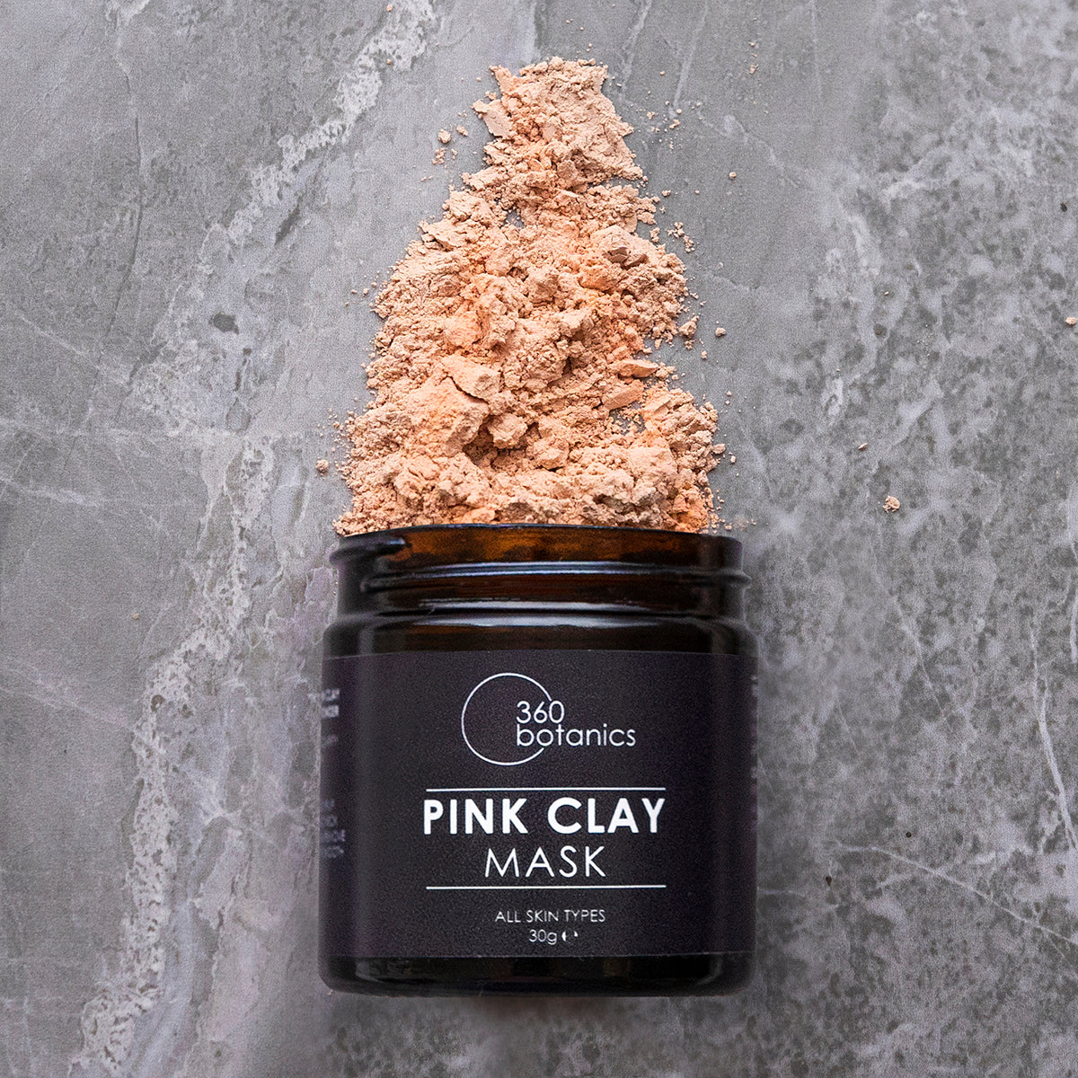 grey marble background, brown jar on its side pink powder coming out top-pink clay