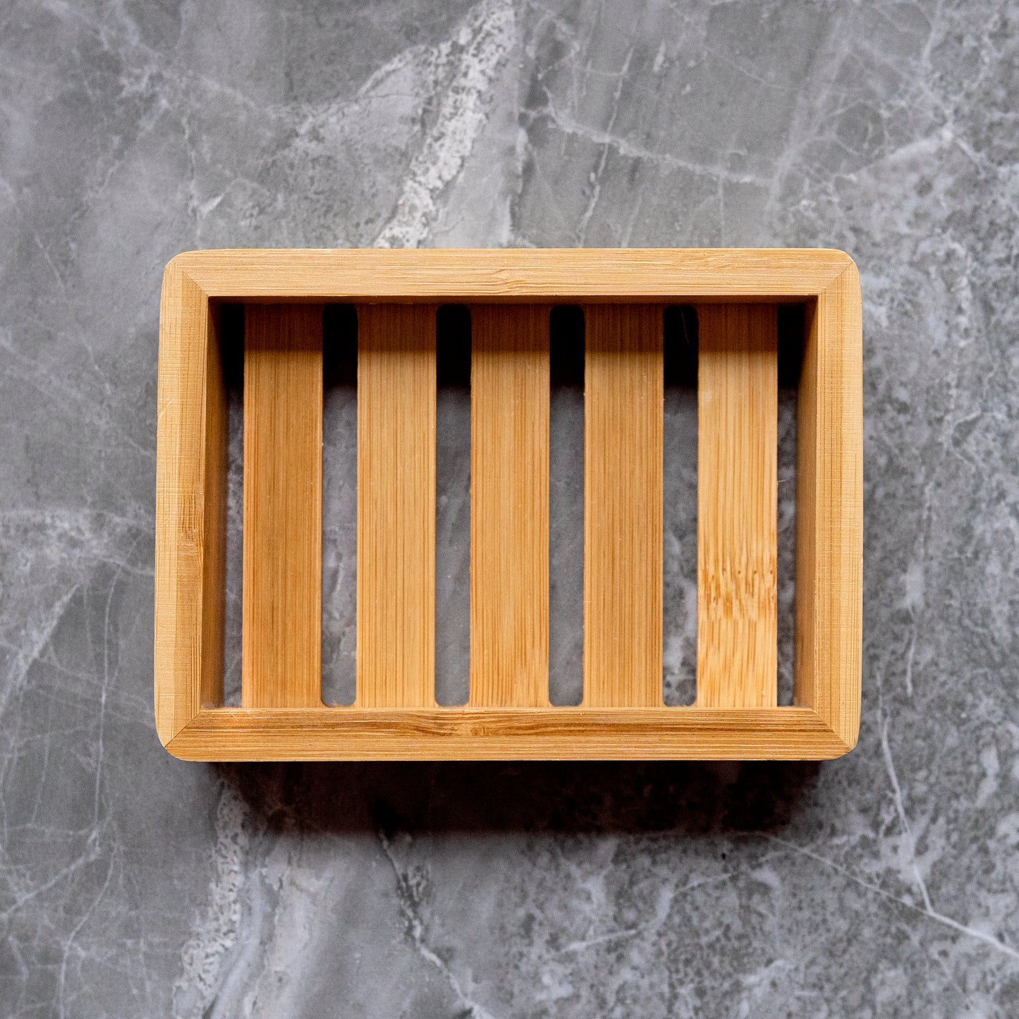 A simple yet elegant bamboo soap dish on a gray marble background. The natural wood tones of the dish contrast beautifully with the cool grey stone, highlighting the eco-friendly and sustainable design ideal for presenting 360 Botanics soap products