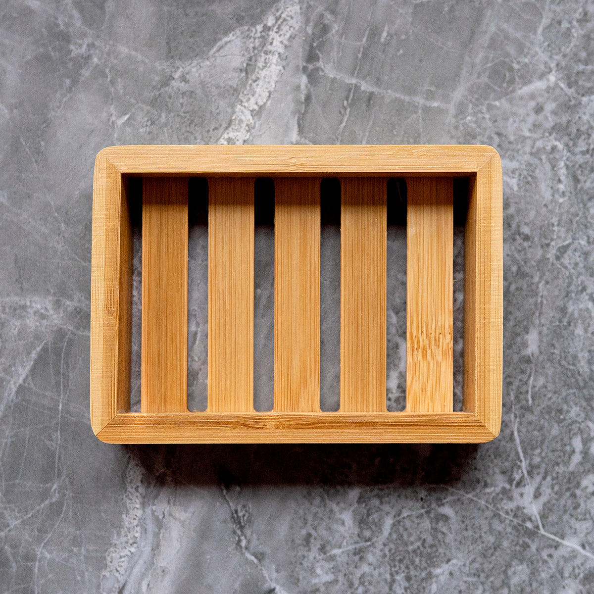 A bamboo soap dish with slats for drainage, viewed from above, set against a grey marble background.