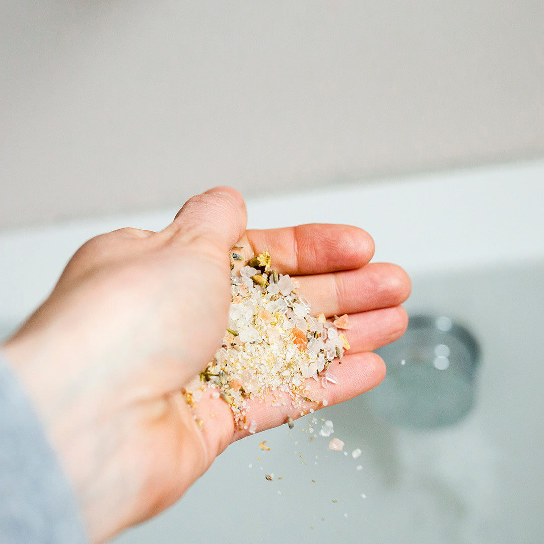 hand held at angle over bath holding bath salts allowing them to fall into bath