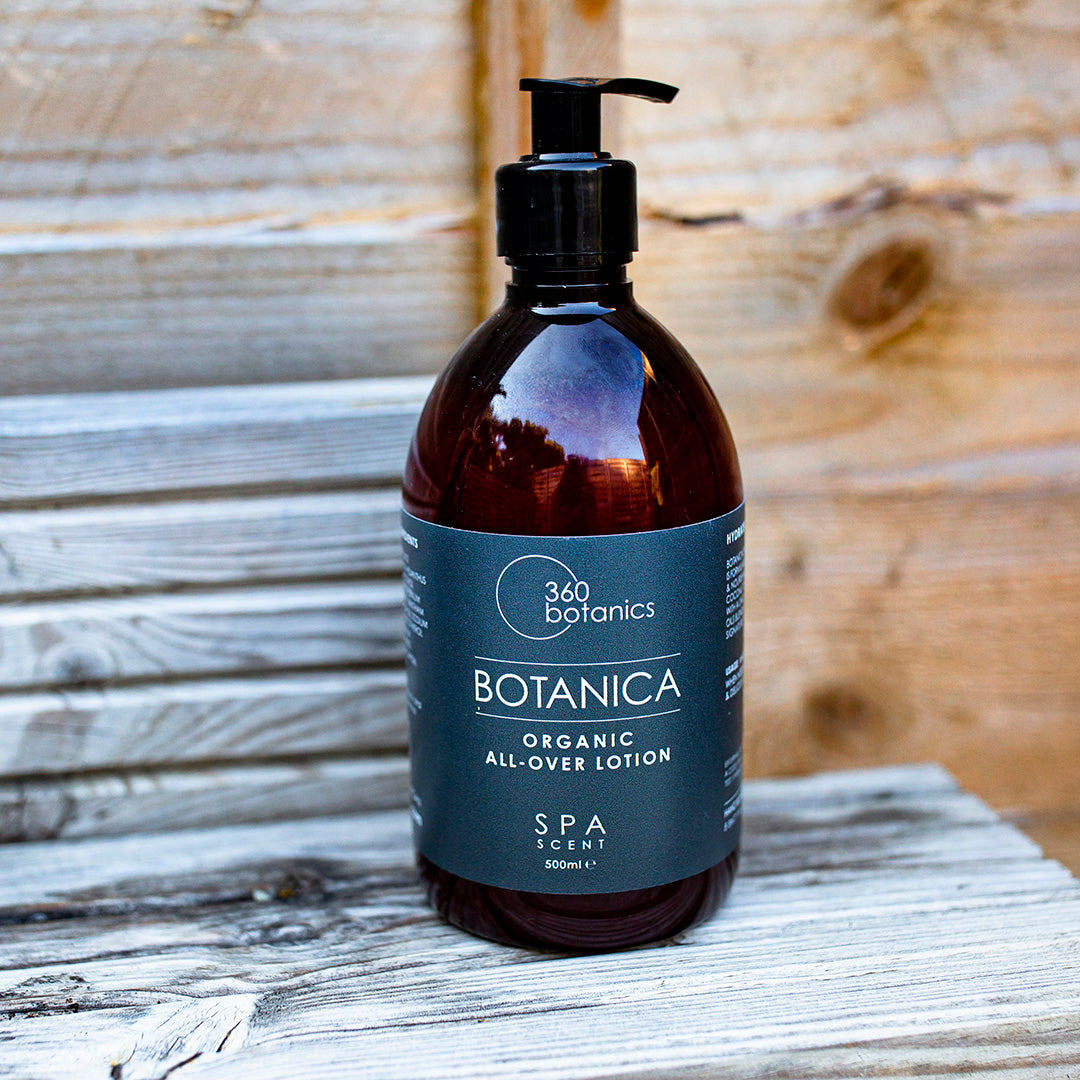 A large bottle of 360 Botanics Botanica Organic All-Over Lotion with a pump dispenser, labeled as "SPA SCENT" in a 500 ml size, standing on a rustic wooden surface with wooden plank background.
