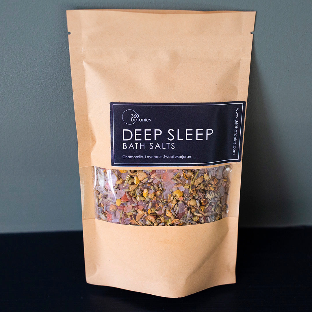 Deep Sleep bath salts sachet on black surface with muted blue coloured wall in background