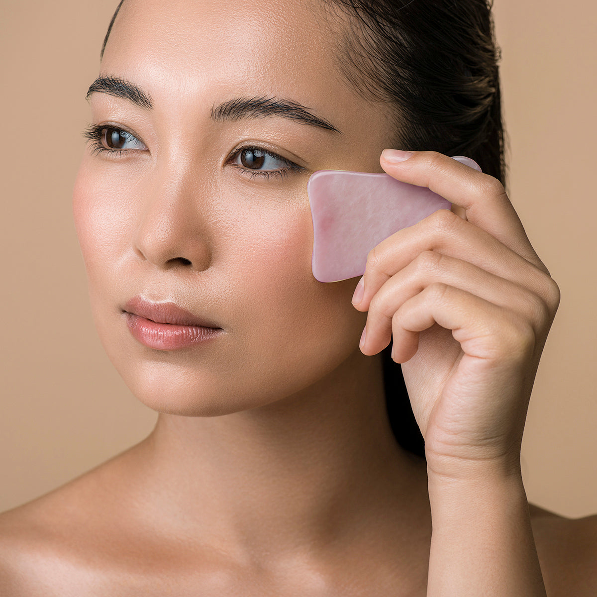 woman using Rose Quartz Gua Sha tool on peach coloured background