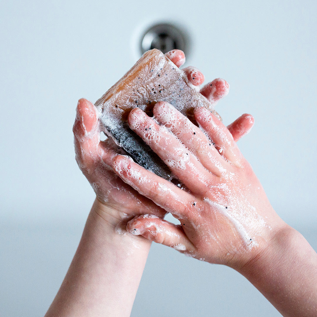 Hands lathering up with a charcoal-based soap from 360 Botanics, creating a rich lather. The image captures the soap in action, demonstrating its cleansing properties, with the focus on the natural and organic skincare benefits offered by the brand