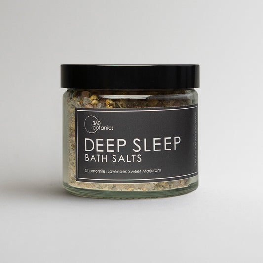 A jar of "360 Botanics Deep Sleep Bath Salts" with a black label detailing ingredients chamomile, lavender, and sweet marjoram on a light background